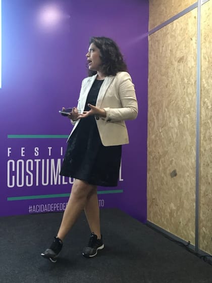 Raisa Arruda em pé apresentando em evento, com projeção ao fundo.